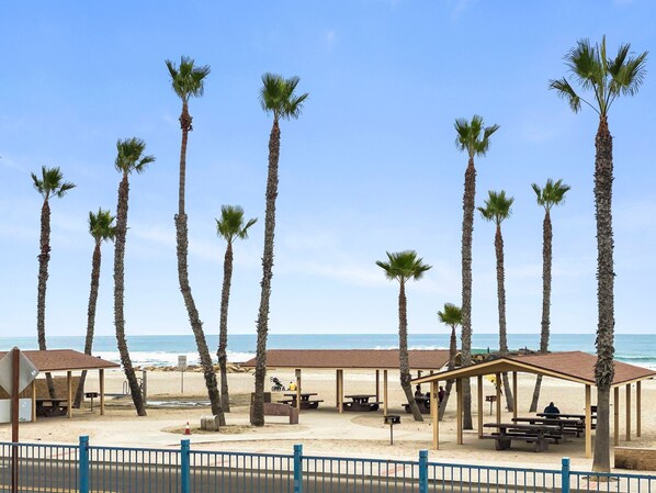 Une plage bordée de palmiers, avec des tables de pique-nique et des espaces de repos abrités.