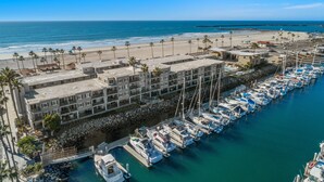 A marina with boats docked, a beach with palm trees, and a building complex with multiple floors.