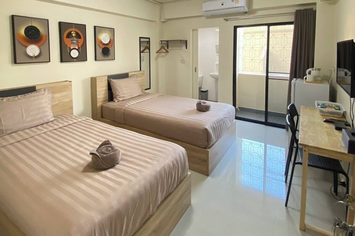 Une chambre d’hôtel avec deux lits, un bureau, une chaise, un appareil de climatisation et une fenêtre avec des rideaux.