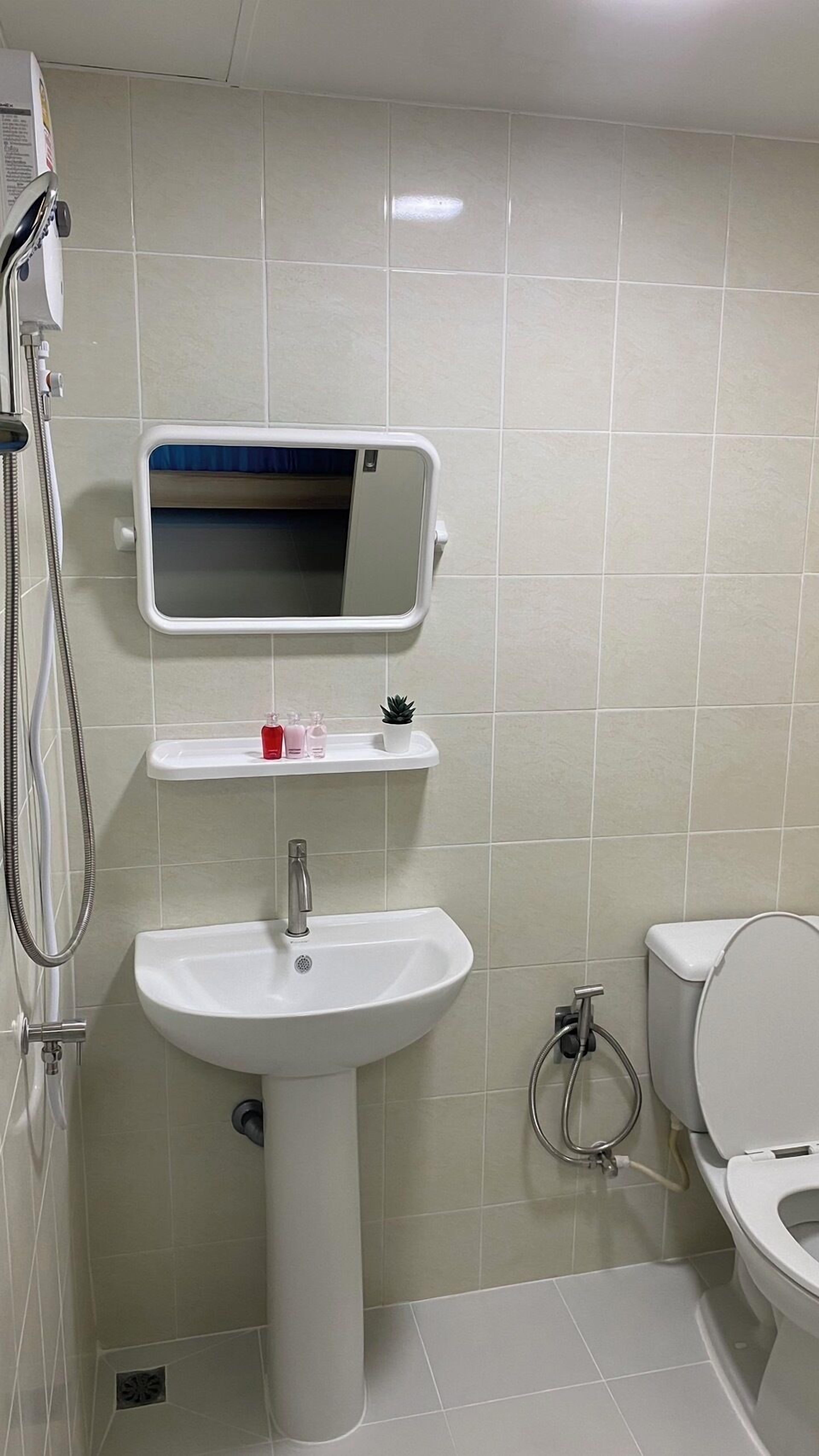 A bathroom with a white sink, a mirror above it, a toilet, and a shower area.