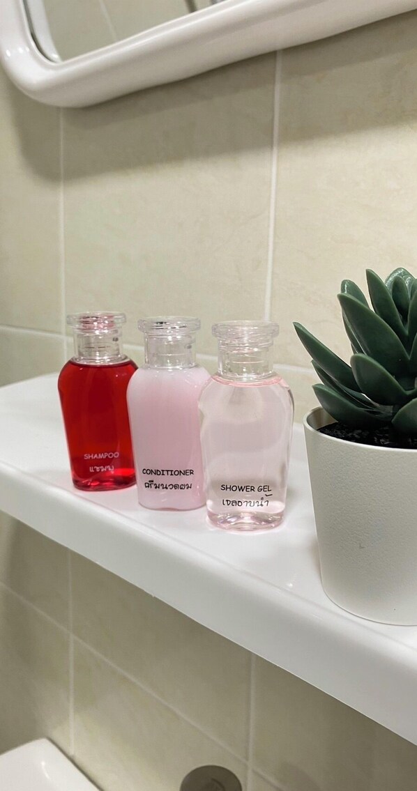 Estante de baño con tres botellas de champú, acondicionador y gel de ducha, además de una suculenta en maceta.