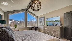 A bedroom with a large bed, a desk, and a dresser. There are large windows with a view of a lake and mountains. - Spacious patio at secluded home in peaceful Deer Valley with private hot tub, BBQ grill (Park City)