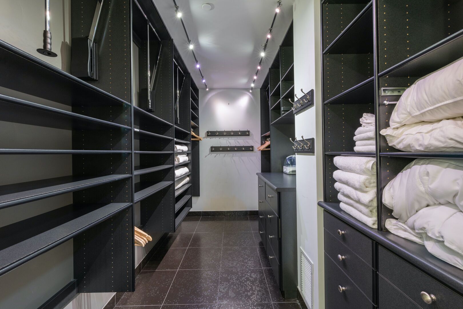 Un vestidor moderno con estanterías negras, un espejo central y toallas dobladas con cuidado.