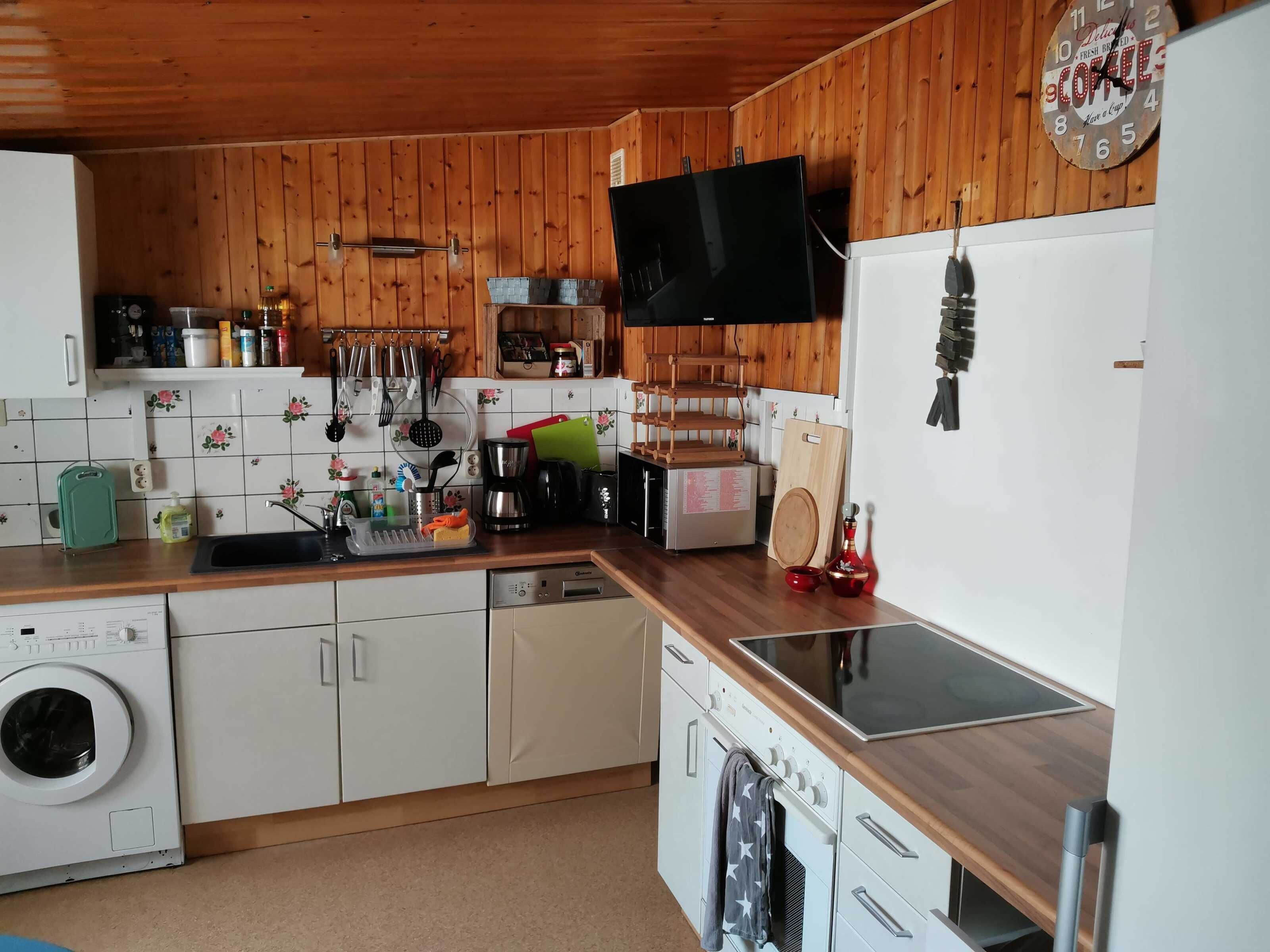 A kitchen with wooden walls, a washing machine, a coffee maker, and a clock.