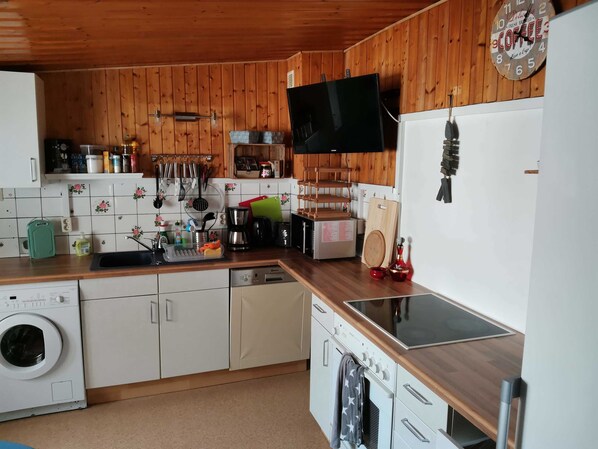 A kitchen with wooden walls, a washing machine, a coffee maker, and a clock.