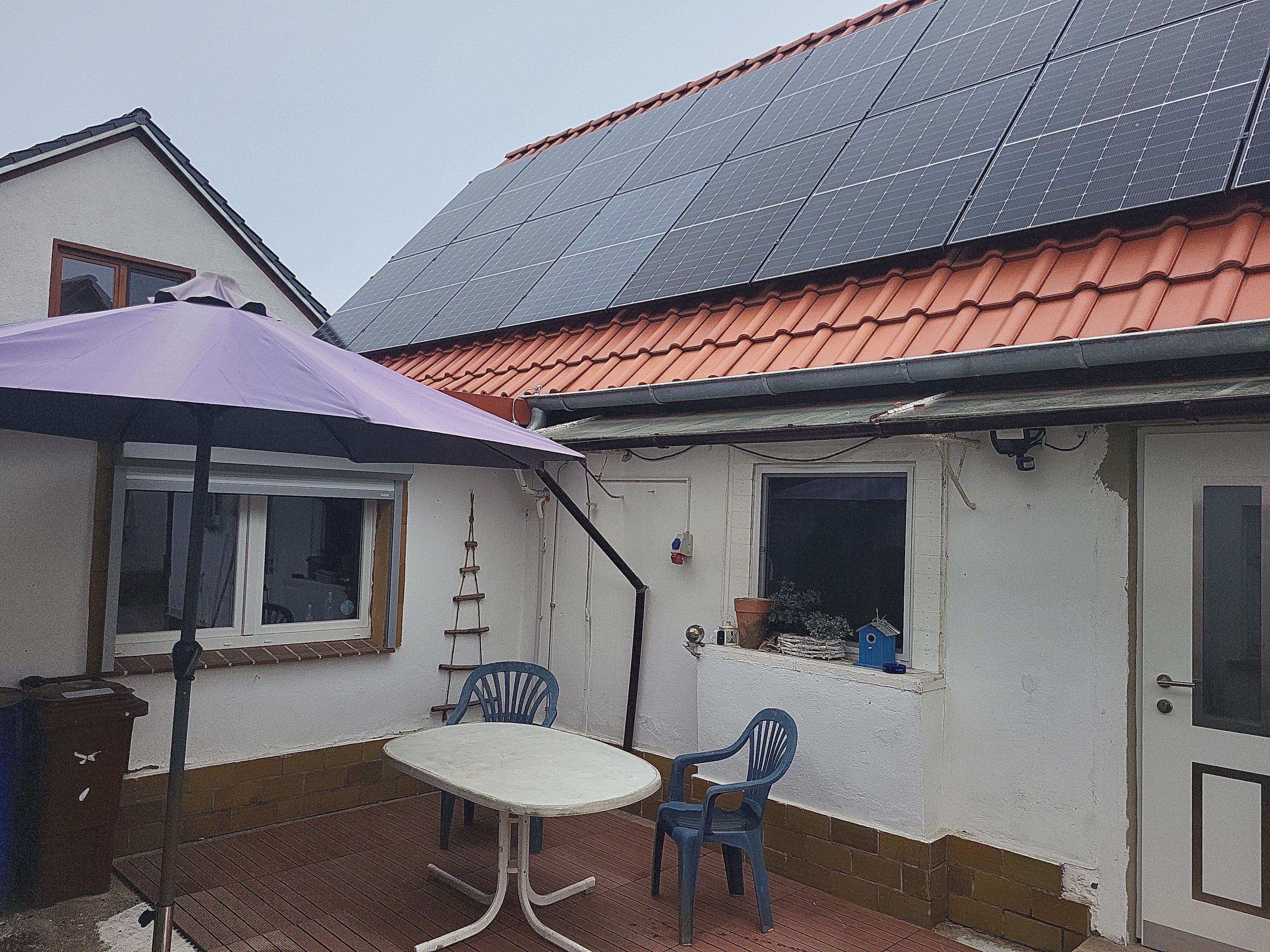Una casa con techo solar, un patio con mesa y sillas, y una ventana pequeña con una planta.