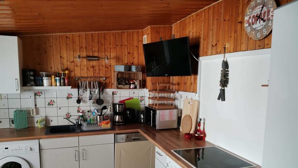 A kitchen with wooden walls, a washing machine, a coffee maker, and a clock. - Fitter and guest house in Groß Rossau - entire house (Osterburg (Altmark))