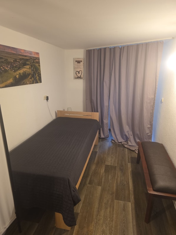 A small, single-bed room with a wooden headboard, a bench, a painting on the wall, and a heart-shaped decoration.