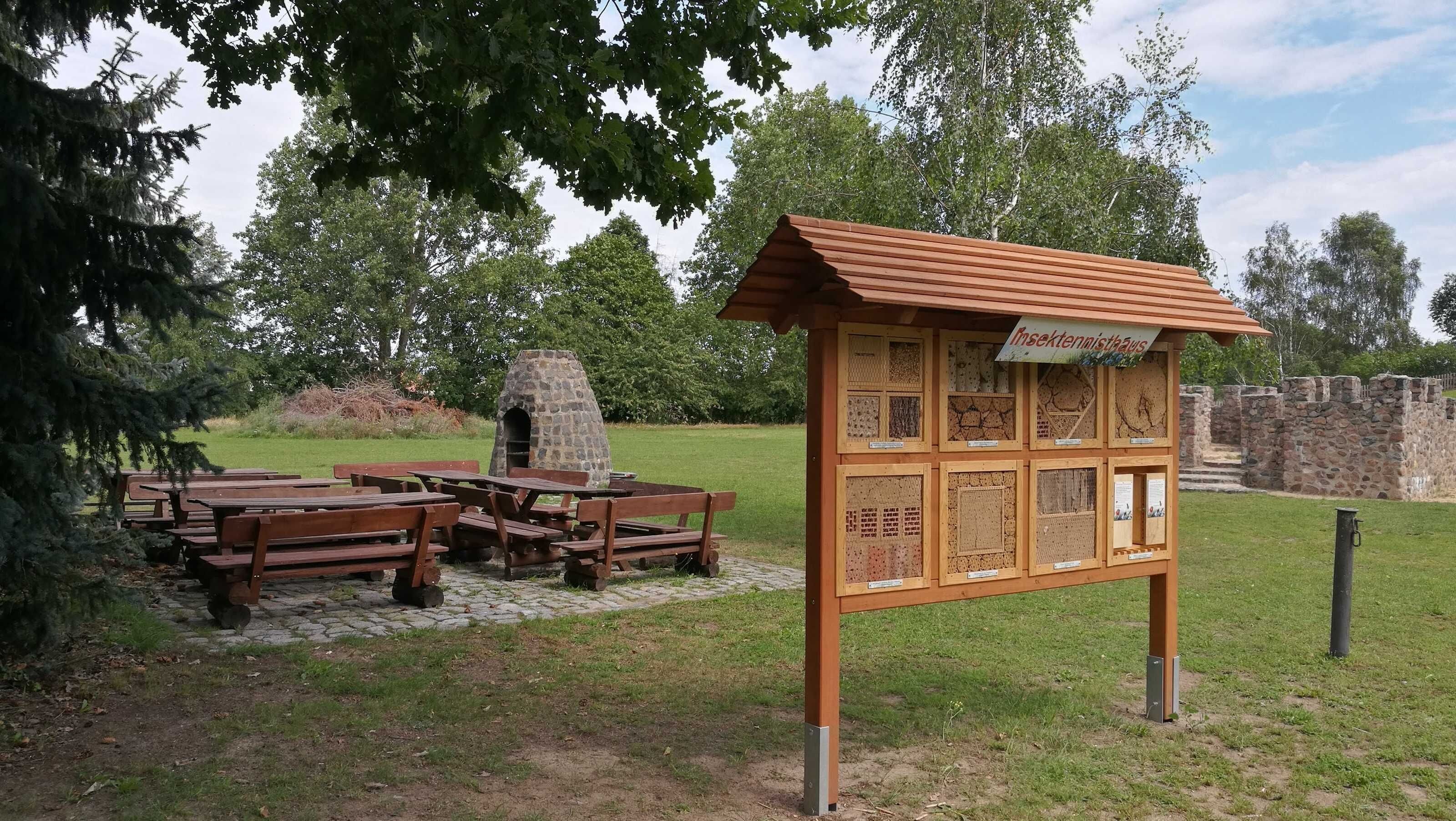 A picnic area with benches and a stone oven, surrounded by a stone wall and trees.