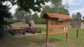 A picnic area with benches and a stone oven, surrounded by a stone wall and trees.