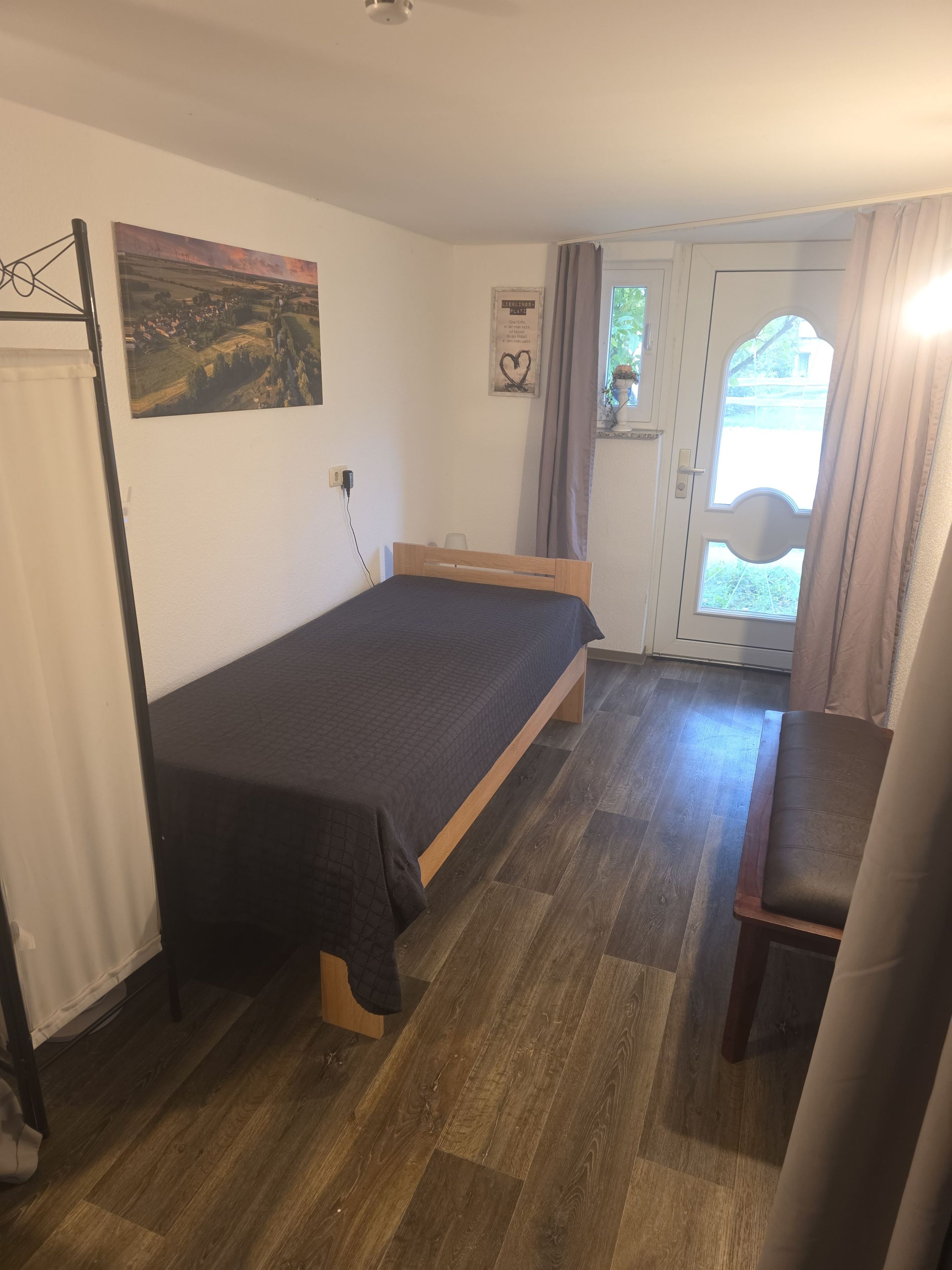 Ein Schlafzimmer mit Bett, Stuhl, Gemälde, Tür und Fenster.