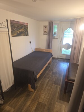 Une chambre à coucher avec un lit, une chaise, un tableau, une porte et une fenêtre.