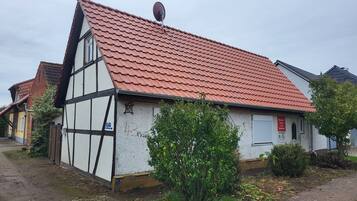 A traditional half-timbered house with a red tiled roof, a satellite dish, and a small garden area.
