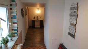Un couloir menant à une cuisine avec un mur recouvert de carreaux, un luminaire fixé au mur et une série de panneaux d’affichage aux messages motivants.