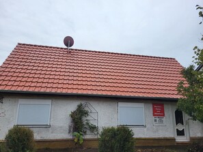 Un bâtiment avec un toit recouvert de tuiles rouges, deux volets blancs, une antenne parabolique et une enseigne indiquant qu’il s’agit d’un restaurant et d’une maison d’hôtes.