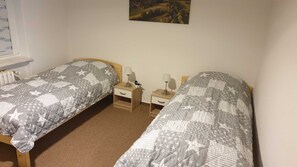 Une chambre avec deux lits simples, chacun recouvert d’une couvre-lit à motifs étoilés, dotée de têtes de lit en bois, de tables de chevet avec des lampes et d’un radiateur fixé au mur.