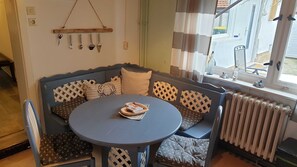 A corner seating area with a table, patterned cushions, and a window with curtains.