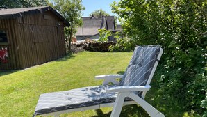 A garden with a lawn, a wooden fence, and a white lounge chair. - Apartment Hohensee ground floor - Ferienwohnung Hohensee (Clausthal-Zellerfeld)
