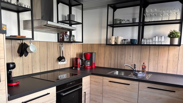 A modern kitchen with wooden cabinets, a black countertop, a built-in oven, a coffee maker, and a sink. - Apartment Hohensee ground floor - Ferienwohnung Hohensee (Clausthal-Zellerfeld)