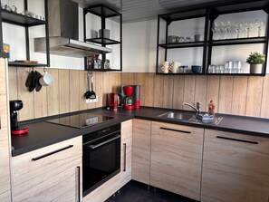 A modern kitchen with wooden cabinets, a black countertop, a built-in oven, a coffee maker, and a sink.