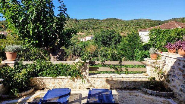 Eine Terrasse mit zwei blauen Lounge-Stühlen, einer Steinmauer und Topfpflanzen.
