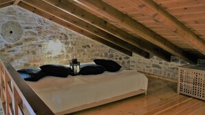 Ein Schlafzimmer mit Steinwand, Holzbalken, einem Bett mit schwarzen Kissen und einer Laterne.