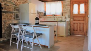 Eine kleine Küche mit Steinwand, Holzbalkendecke, einem weißen Kühlschrank, einer Spüle, einem Geschirrspüler und zwei Barhocker.