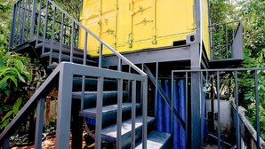 A yellow shipping container converted into a small structure with a staircase leading to a platform. - Hip's House Homestay - Hostel (Phu Quoc)