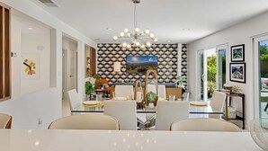 Ein moderner Essbereich mit einem zentralen Tisch, Stühlen, einer Deckenleuchte und einem an der Wand befestigten Fernseher.