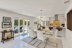 A modern kitchen with a central island, a dining area with a glass table, and a view of a pool through the sliding doors. - Poolside Palms: Great Pool, Bocce Ball, Firepit (palm springs)