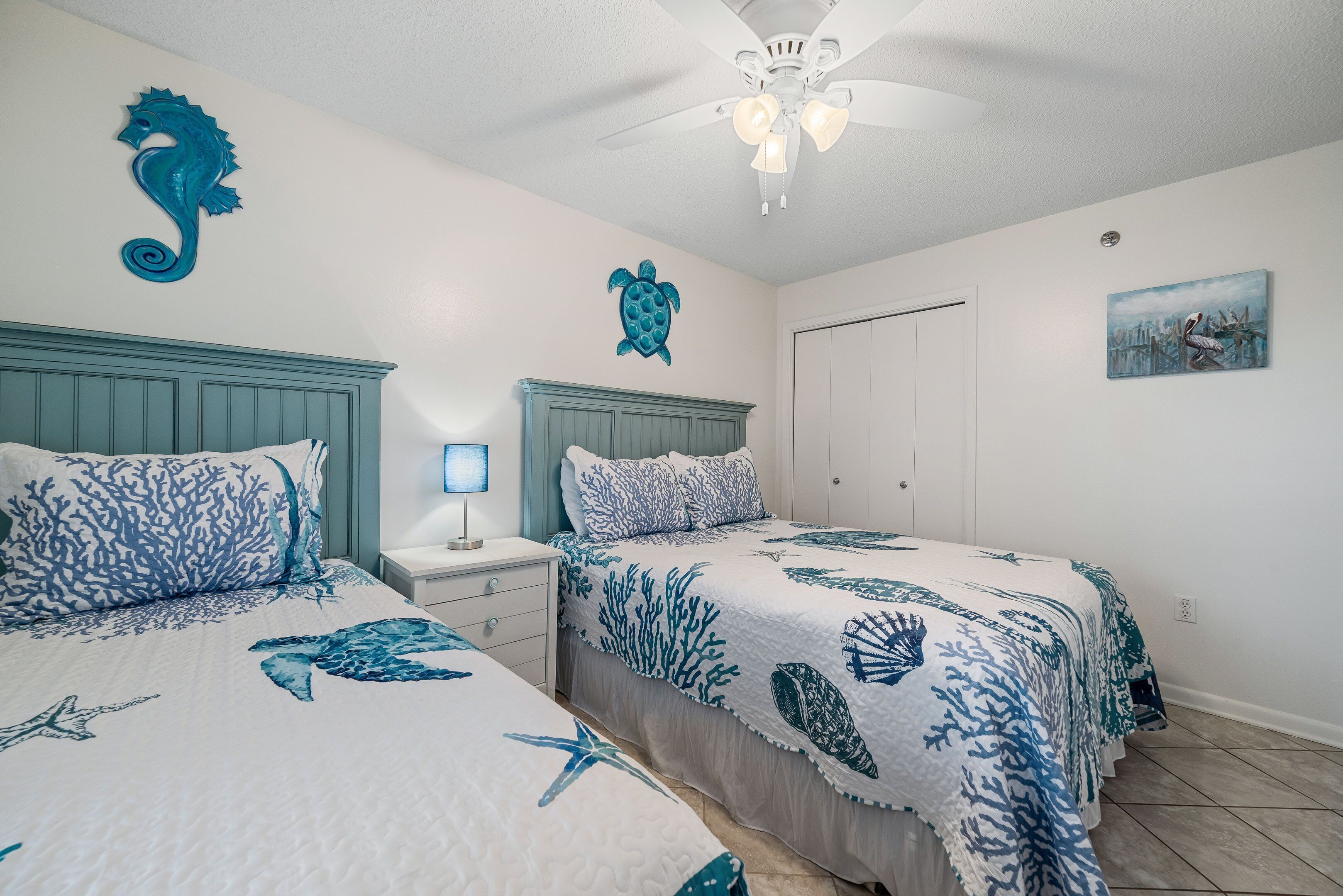 A bedroom with two beds, a ceiling fan, and wall art.