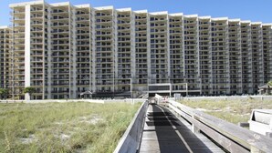 A high-rise hotel with multiple balconies and a boardwalk leading to the entrance. - Phoenix VII 212 | Beachfront | Heated Indoor Pool | My Beach Getaways (Orange Beach)