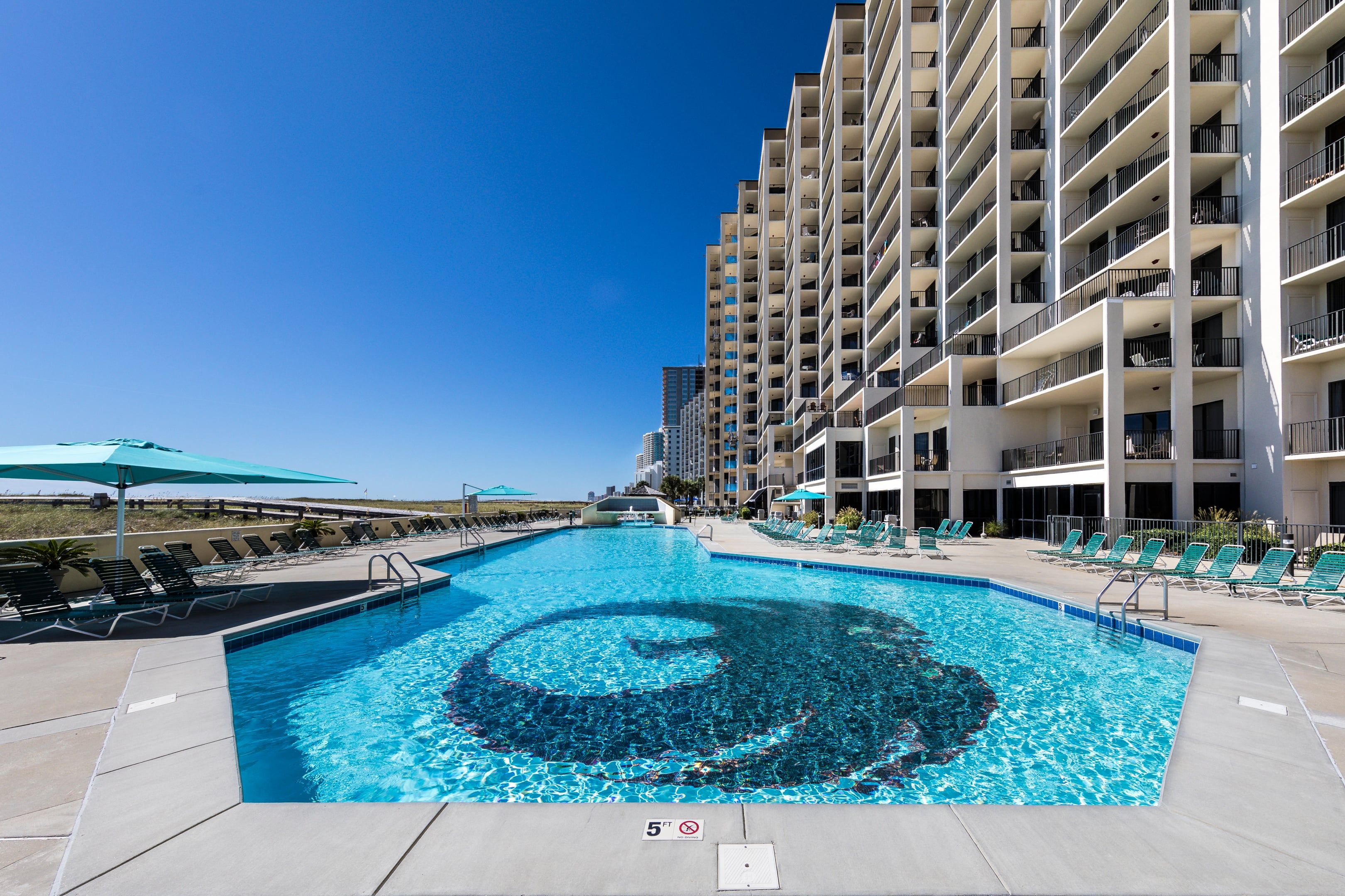 A swimming pool with a circular design, surrounded by lounge chairs and a multi-story building with balconies.