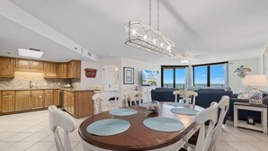 A spacious kitchen with wooden cabinets, a dining table with white chairs, and a large window offering a view. - Phoenix VII 212 | Beachfront | Heated Indoor Pool | My Beach Getaways (Orange Beach)
