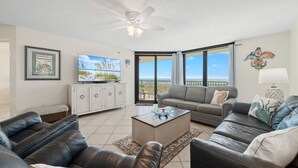 A living room with leather sofas, a coffee table, a TV, and a balcony with a view of the ocean. - Phoenix VII 212 | Beachfront | Heated Indoor Pool | My Beach Getaways (Orange Beach)