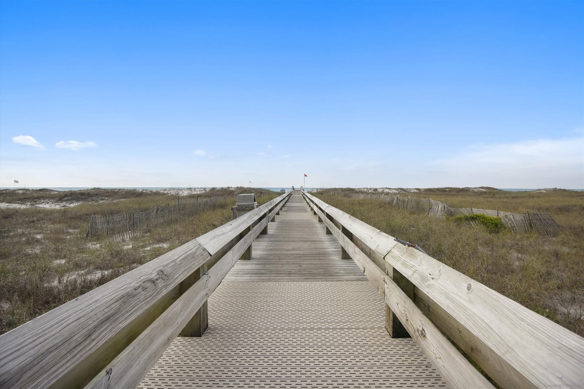 Une promenade en bois menant à une plage bordée de dunes, sous un ciel dégagé.