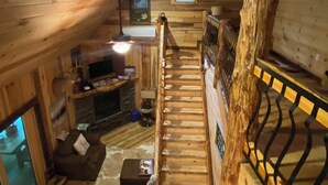 L'interno di una baita in legno con una scala, un camino, una televisione e un'accogliente area salotto.