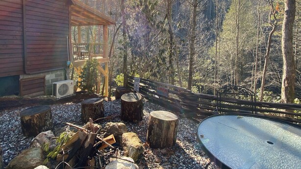 Un'area salotto esterna rustica con un fuoco, circondata da rocce e alberi.