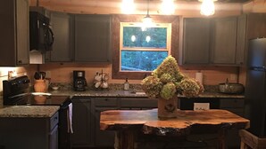 Una cucina rustica con mobili in legno, un'isola centrale con base in pietra e una finestra con vista sugli alberi.