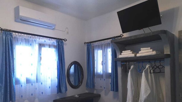 A bedroom with a bed, a desk, a chair, a TV, and a wardrobe with towels. -       BLUE SUITE     (Santorini)