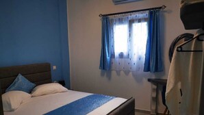 A bedroom with a bed, a bedside table, a hanging towel, and a window with curtains. -       BLUE SUITE     (Santorini)