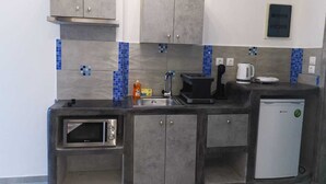 A compact kitchen with grey cabinets, a built-in microwave, a coffee maker, and a small refrigerator. -       BLUE SUITE     (Santorini)