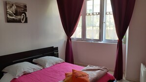 Une chambre à coucher avec un lit, deux oreillers, une couvre-lit rose, une fenêtre avec des rideaux et un tableau au mur.