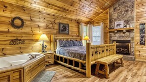 Ein Schlafzimmer in einer Blockhütte mit einem hölzernen Bett, einem Kamin aus Stein, einer Badewanne und einer Bank.
