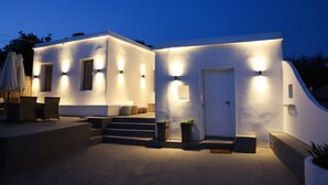 Un edificio moderno con iluminación exterior, una puerta y escalones que conducen a un área cubierta con mobiliario.