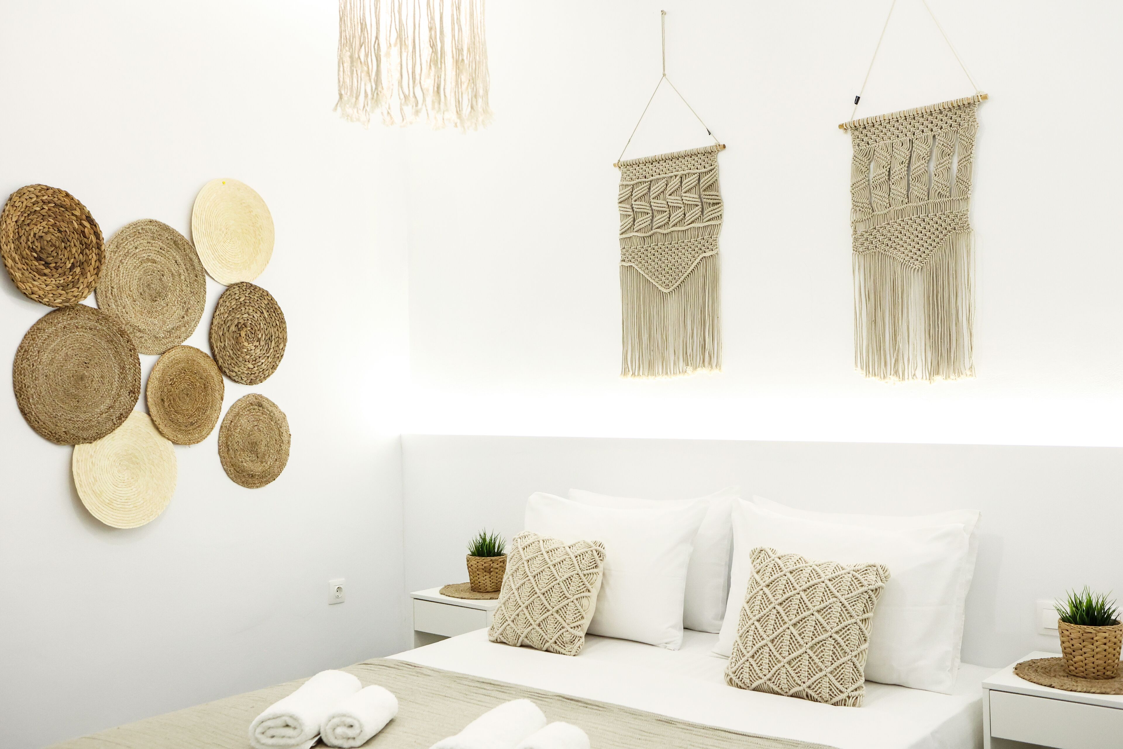 Une chambre à coucher au style minimaliste, avec un lit, du linge de lit blanc et des éléments décoratifs en tissu accrochés au mur.