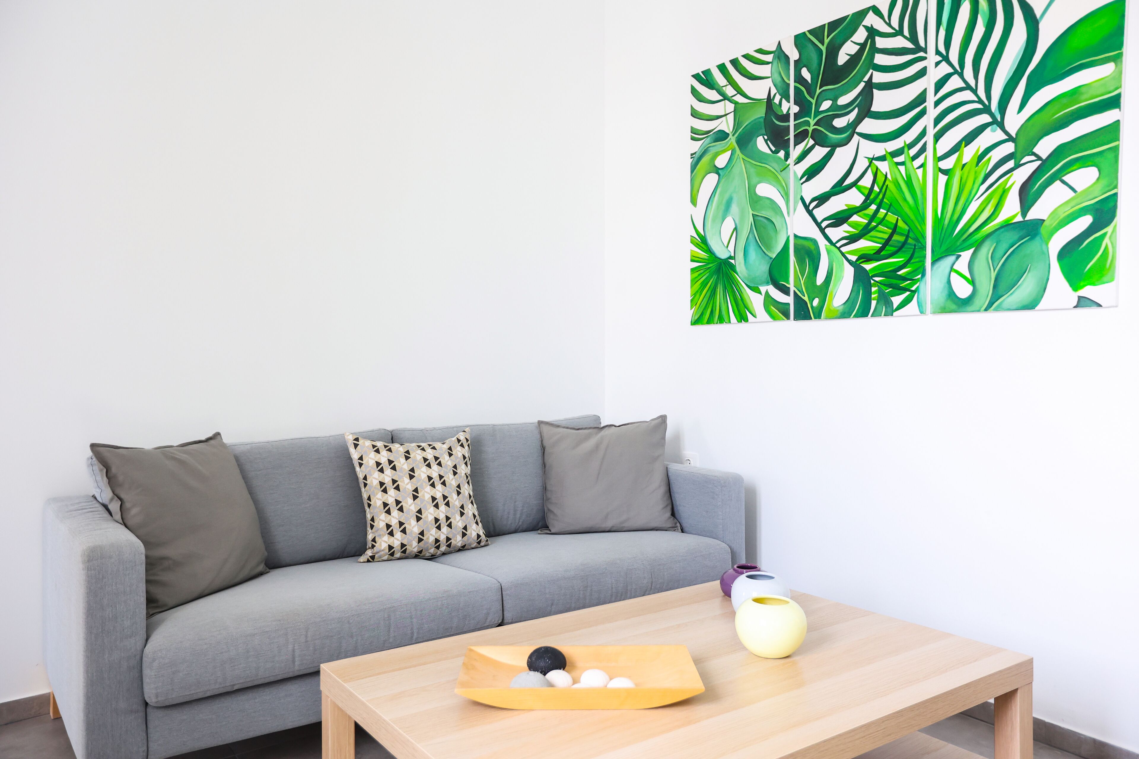 Una sala de estar moderna con un sofá gris, una mesa de centro de madera y una obra de arte en la pared.