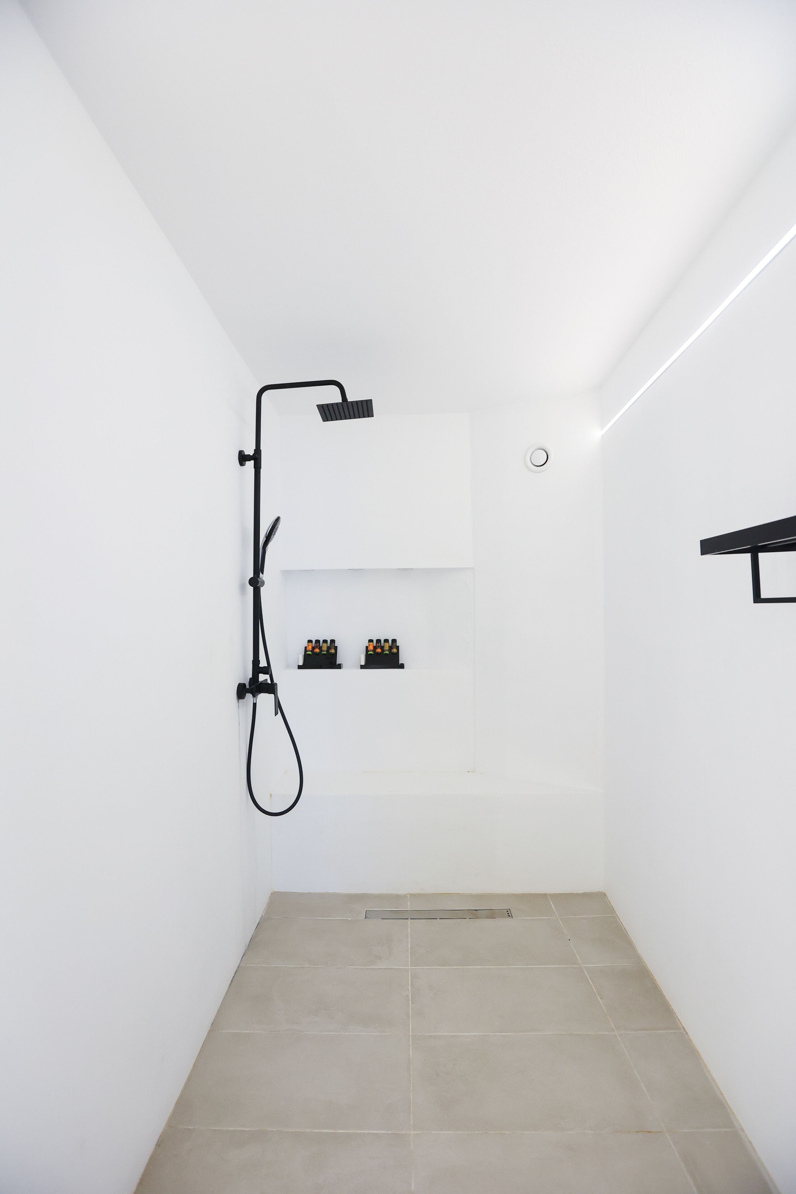 Un baño pequeño y moderno con ducha, un estante con artículos de aseo y un perchero para toallas.