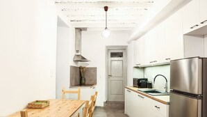 Una cocina moderna con armarios blancos, un refrigerador de acero inoxidable, una mesa de comedor de madera y una lámpara colgante.