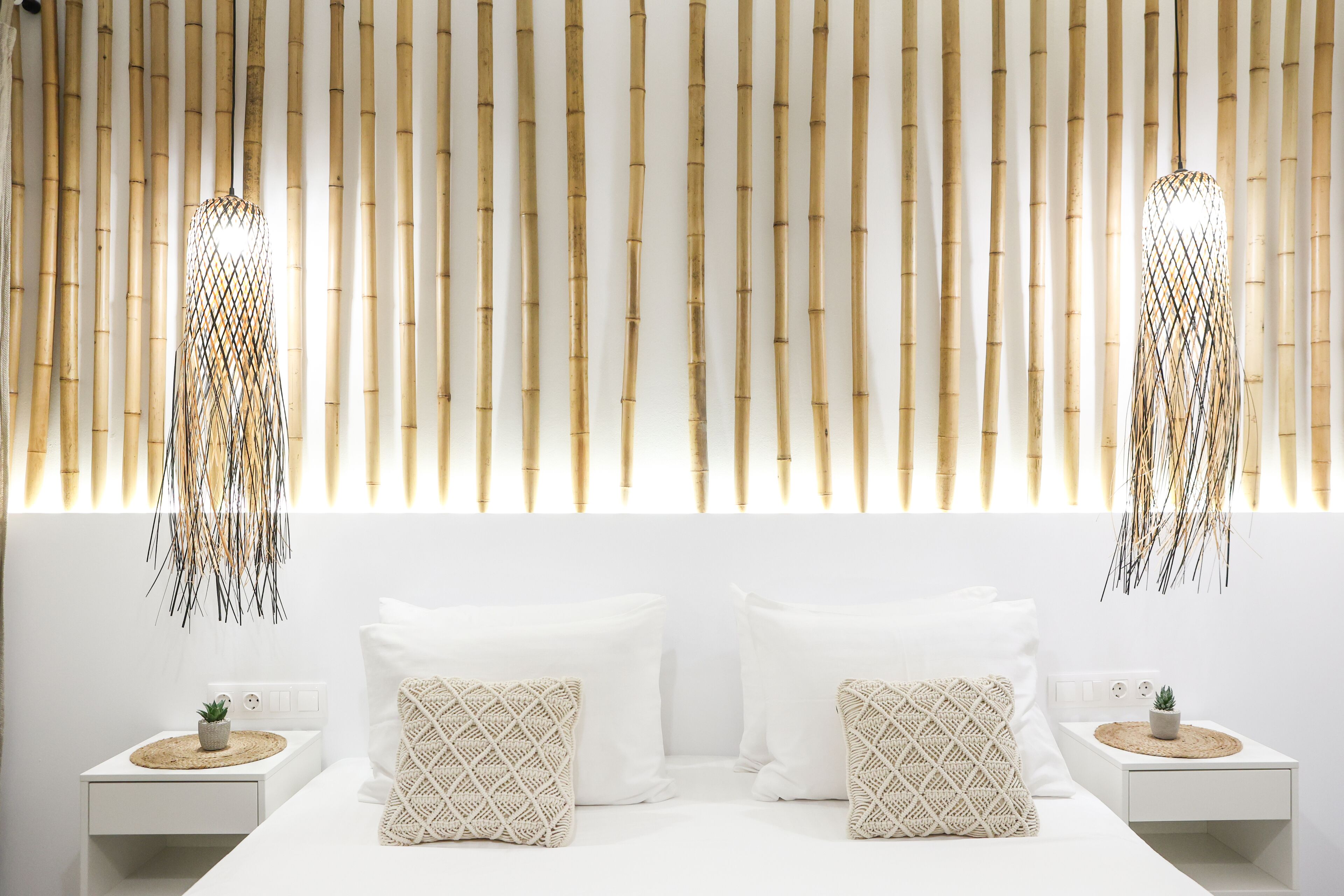 A modern bedroom with a white bed, two nightstands, and a bamboo wall panel.